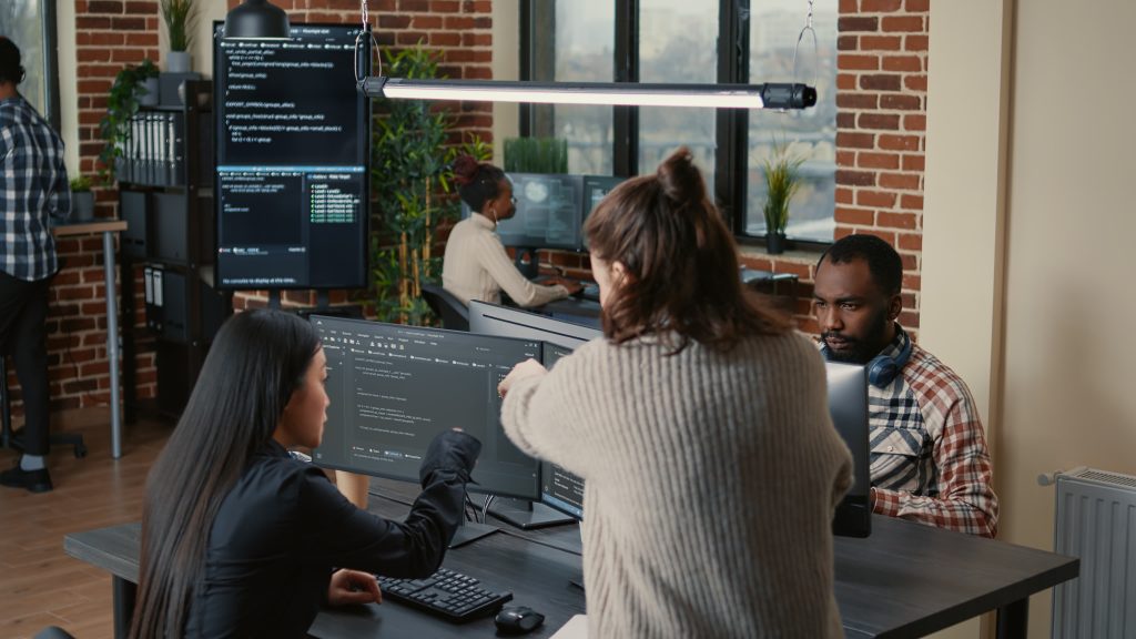 Programador aponta para o código e explica o algoritmo a um colega, o julgamento humano que mostra por que a inteligência artificial não vai substituir programadores.