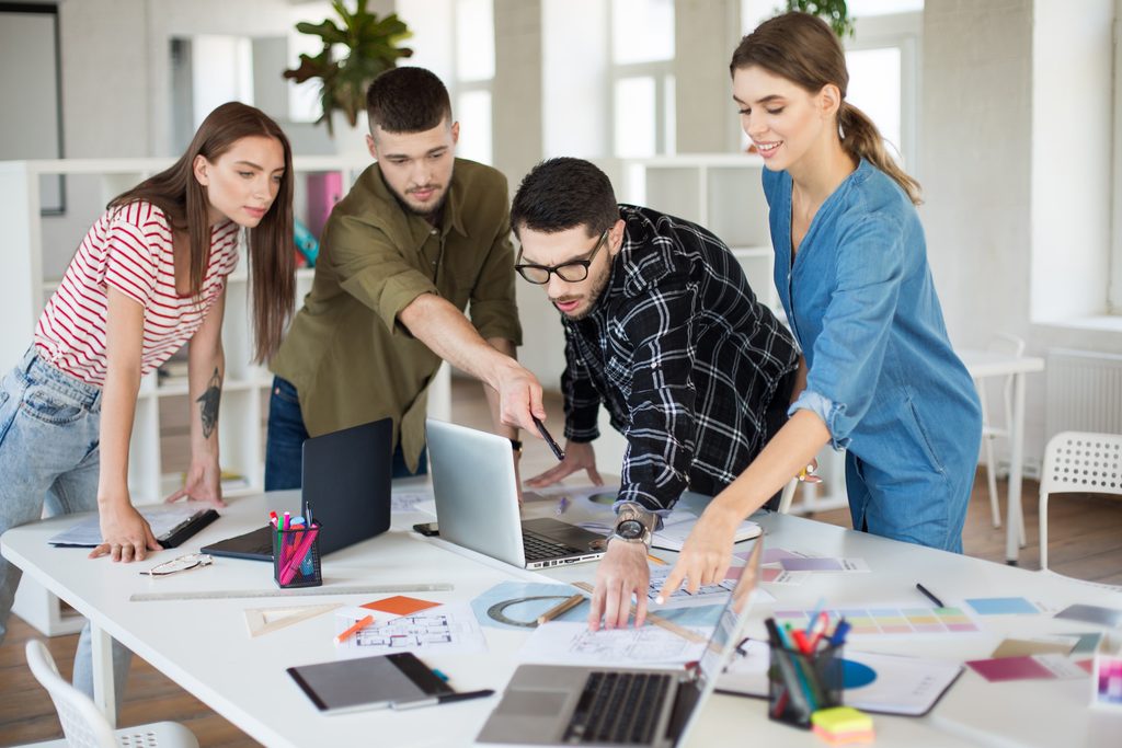 Grupo de estudantes universitários reunidos com laptop e anotações na biblioteca do campus, representando a formação como caminho de prevenção contra a falha de projetos.